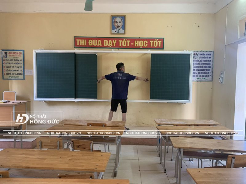 Thợ lắp đặt đo hệ bảng trượt ba tấm vừa gắn lên tường lớp học