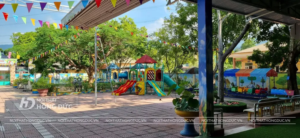 Sân trường có khu đồ chơi ngoài trời dưới tán cây